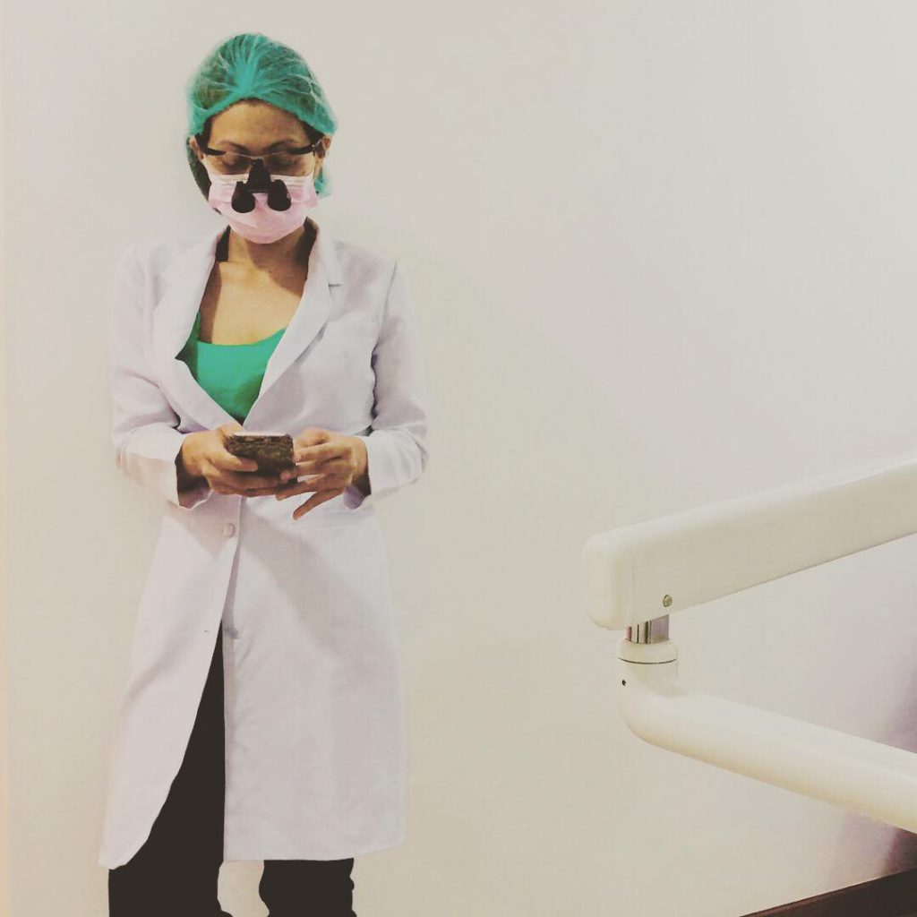 The dentist looking at her phone, while wearing magnifying lenses after a treatment